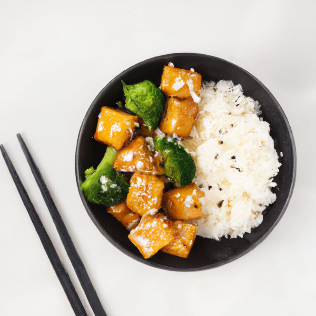 Savory Asian-inspired dish with roasted squash, broccoli, and cauliflower served with fluffy white rice in a black bowl. Perfect for healthy meal options and plant-based diets.