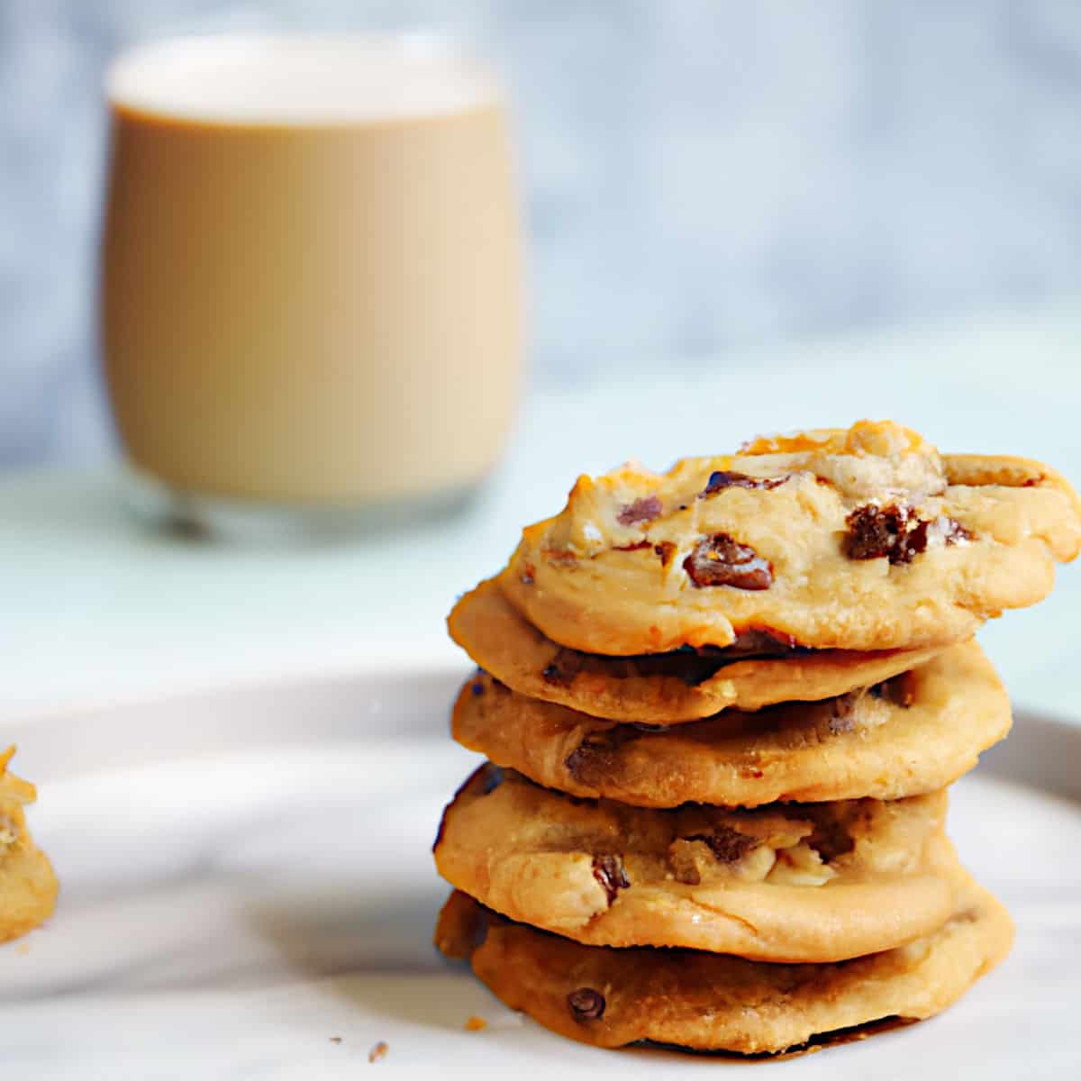Rich chocolate chip cookies stacked with a glass of milk in the background, showcasing homemade baked goods perfect for snacking or dessert.