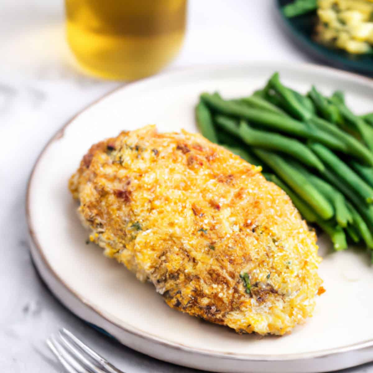 Crispy breaded chicken breast with melted cheese served with fresh green beans on a white plate. Perfect comfort food meal, ideal for dinner or lunch, showcasing delicious baked or fried chicken.