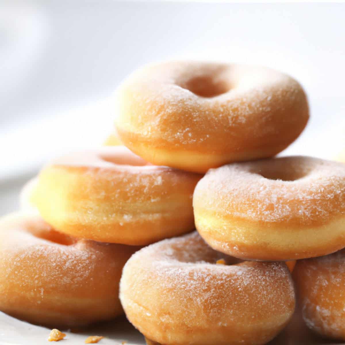 Soft powdered sugar-coated donuts stacked, with a close-up view highlighting their golden-brown texture, ideal for sweet treat visuals or bakery product presentations.